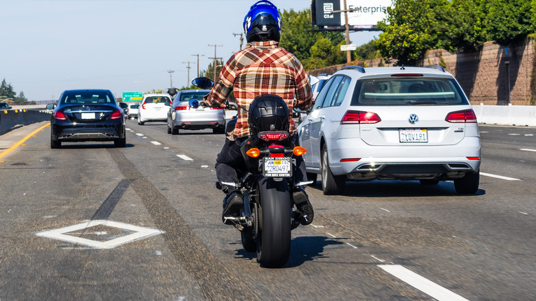 A motorcycle rider riding on the HOV lane behind a black Mercedes-Benz