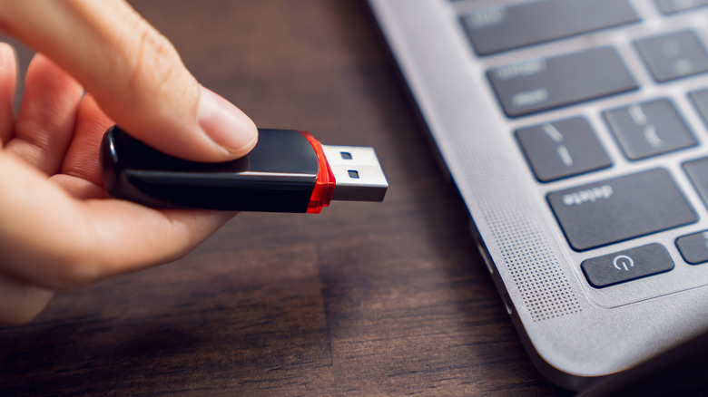 Hand holding usb flash drive with connecting to laptop at wooden table